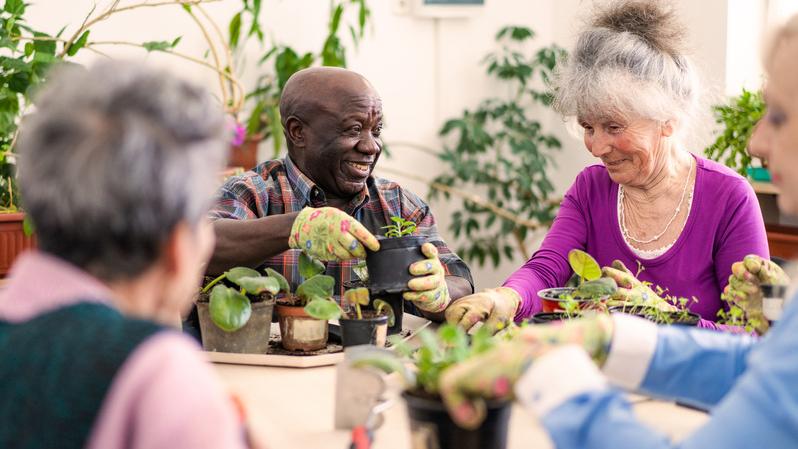 Group of adults enjoying a gardening activity, smiling and potting plants