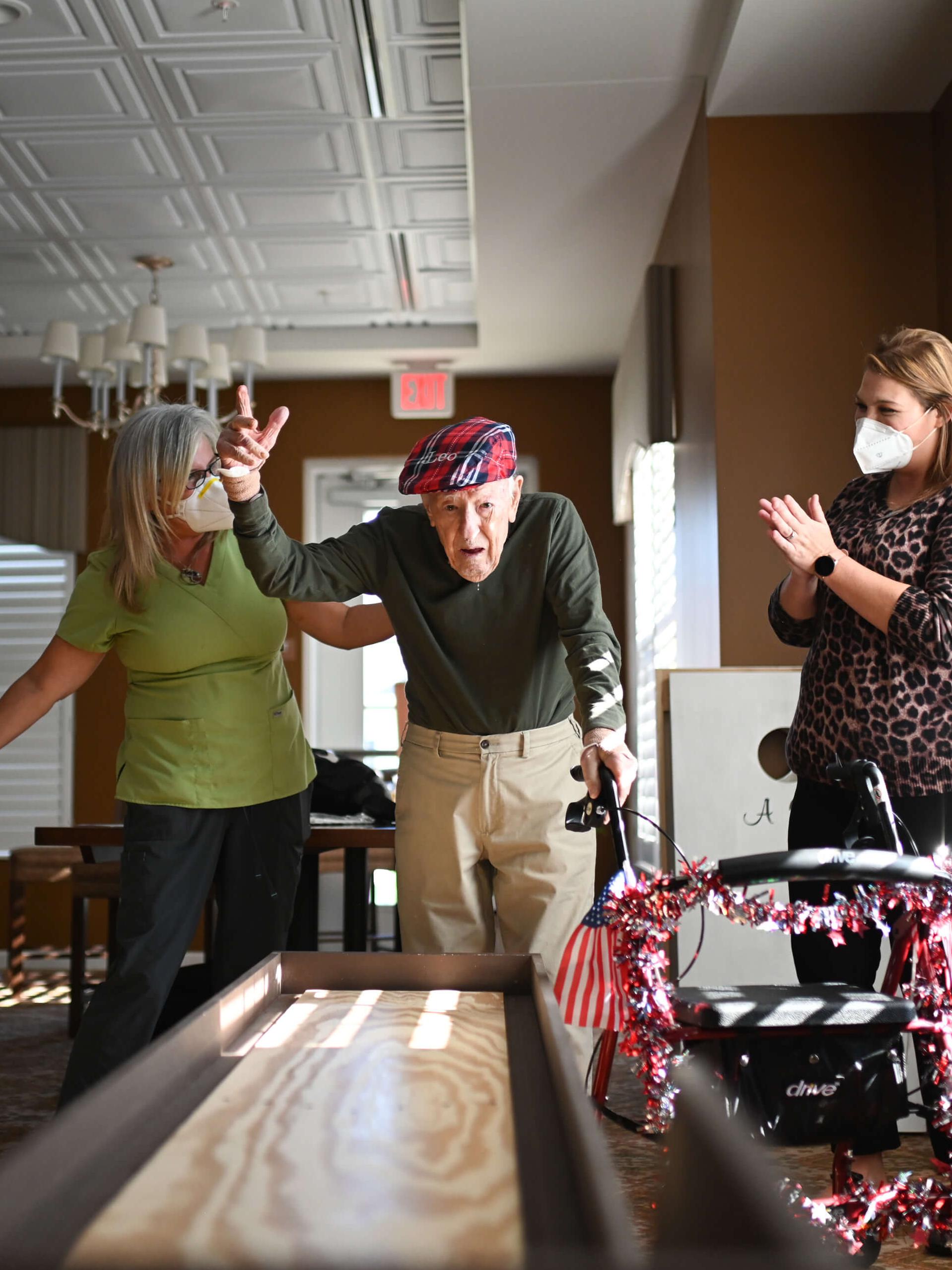 resident playing shuffle board with two women cheering him on