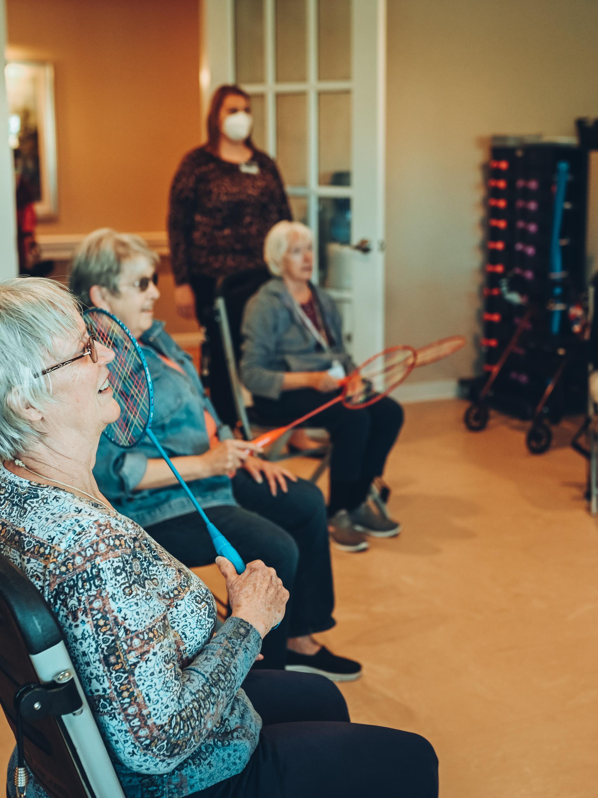 People participating in a seated group exercise class with rackets and a fitness instructor