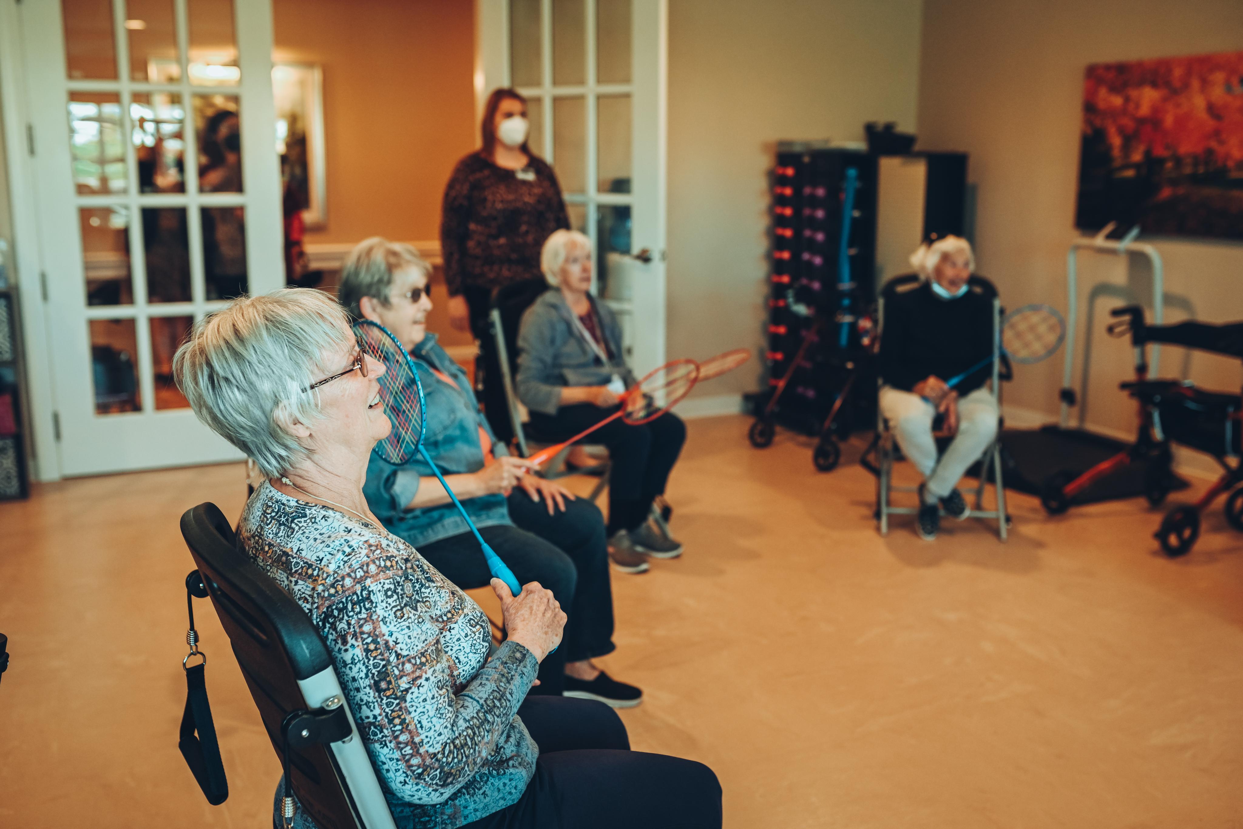 People participating in a seated group exercise class with rackets and a fitness instructor