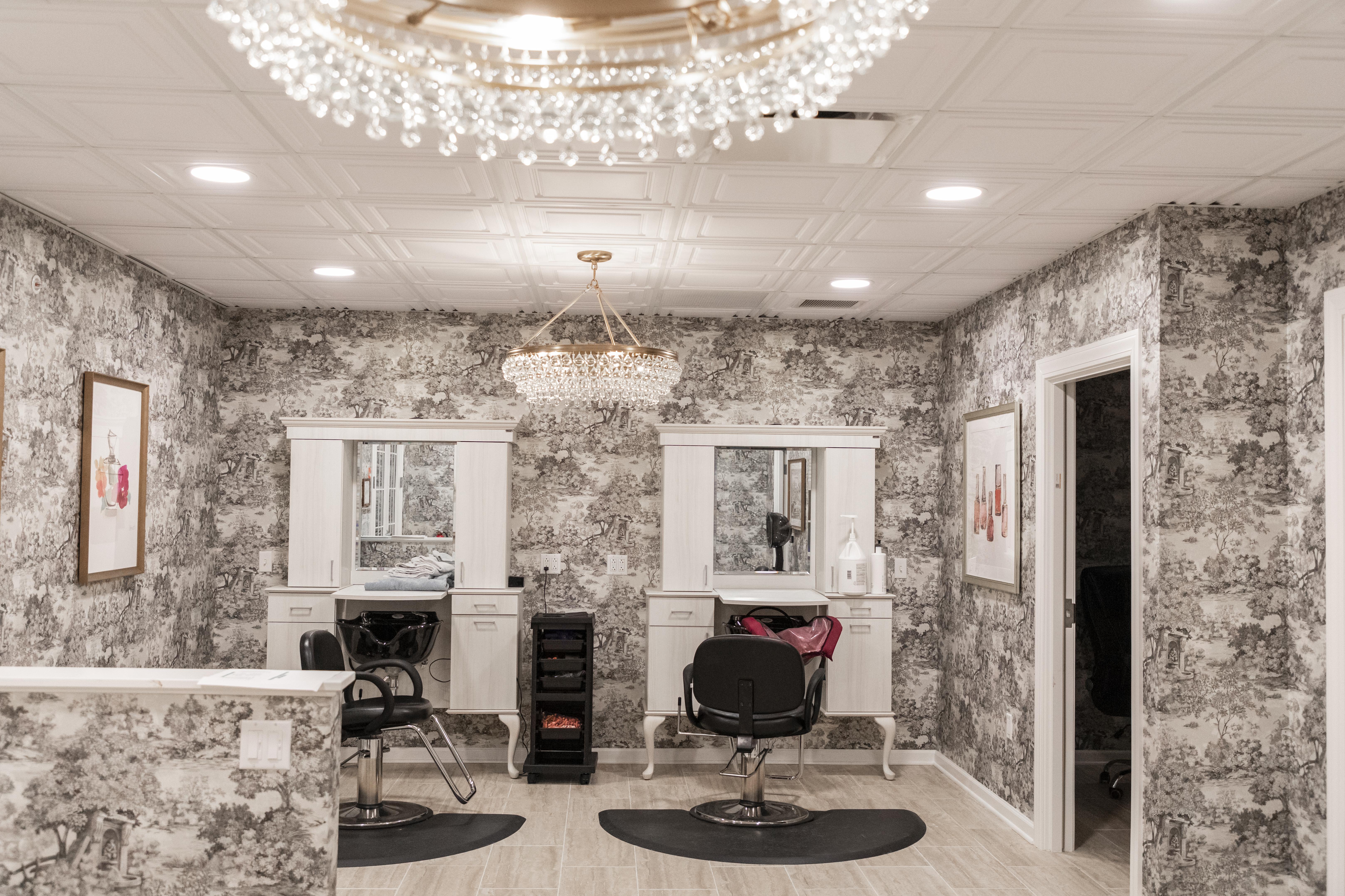 Stylish hair salon interior with ornate chandeliers, floral wallpaper, and salon chairs