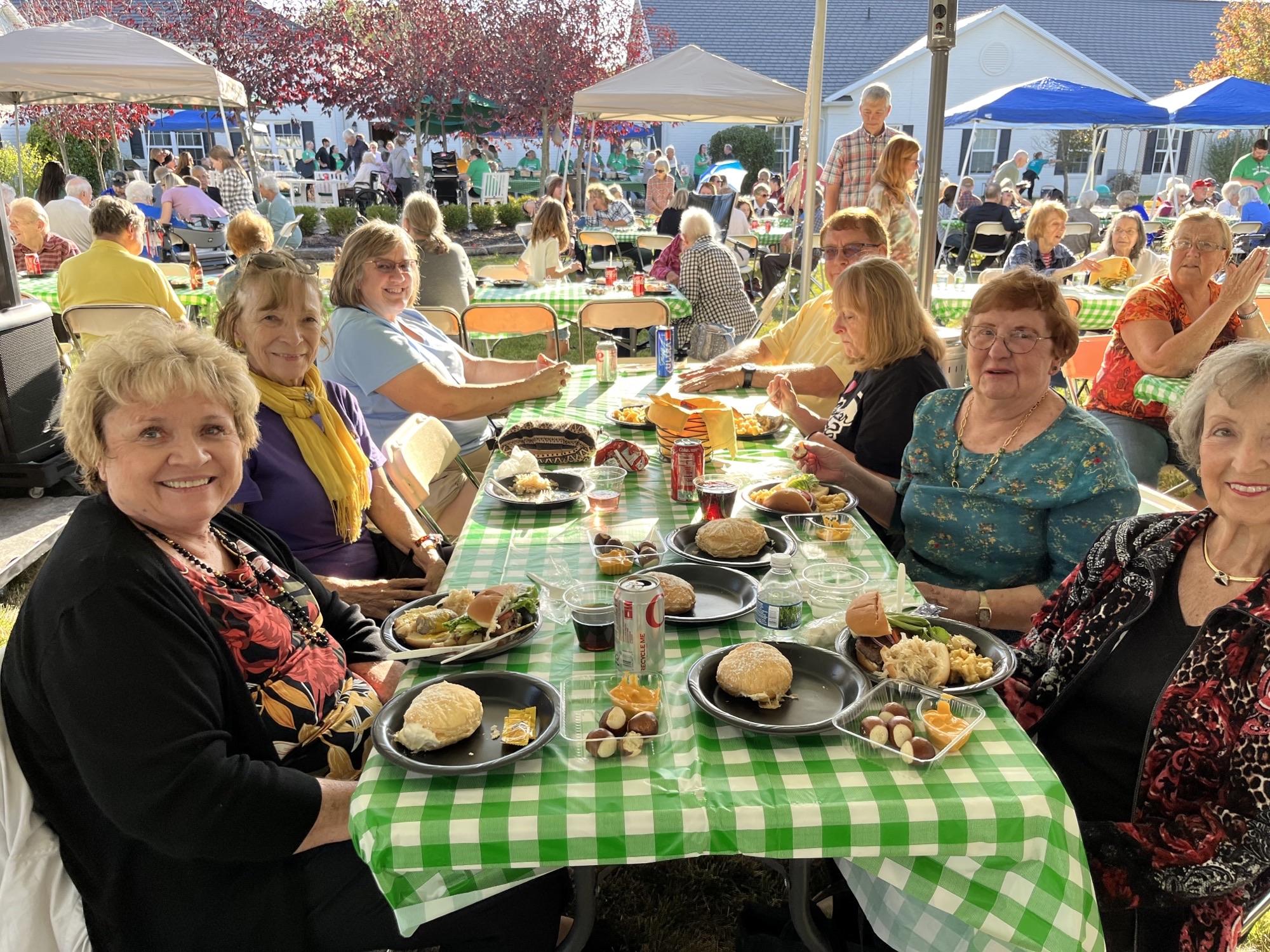 Happy people enjoying an outdoor picnic with a green checkered tablecloth and food