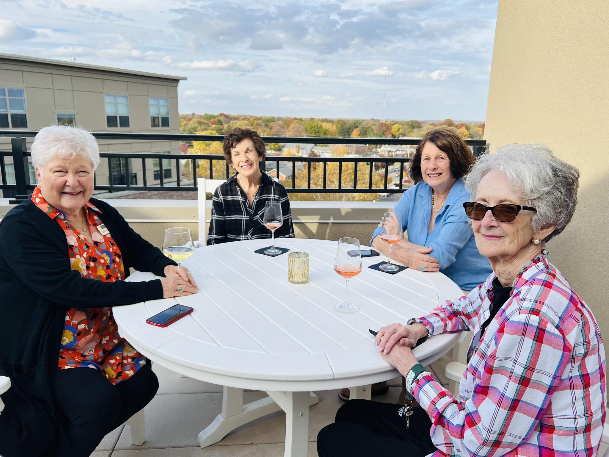 Four women sitting around a white patio table, enjoying a conversation outdoors.