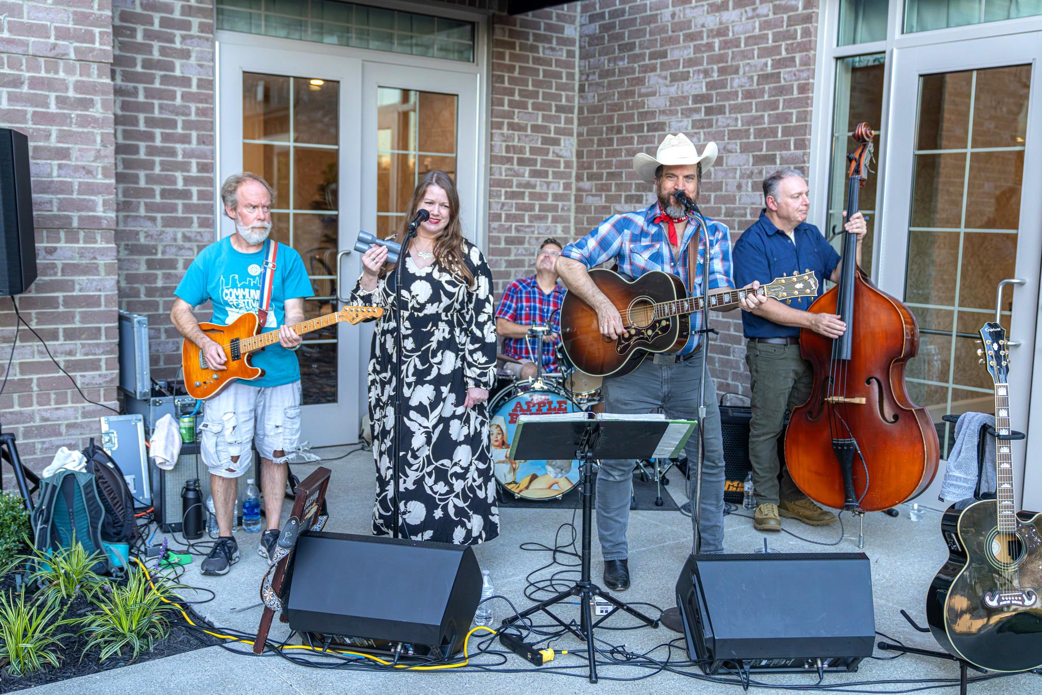 Band with four musicians playing a guitar, singing, and playing a double bass outdoors