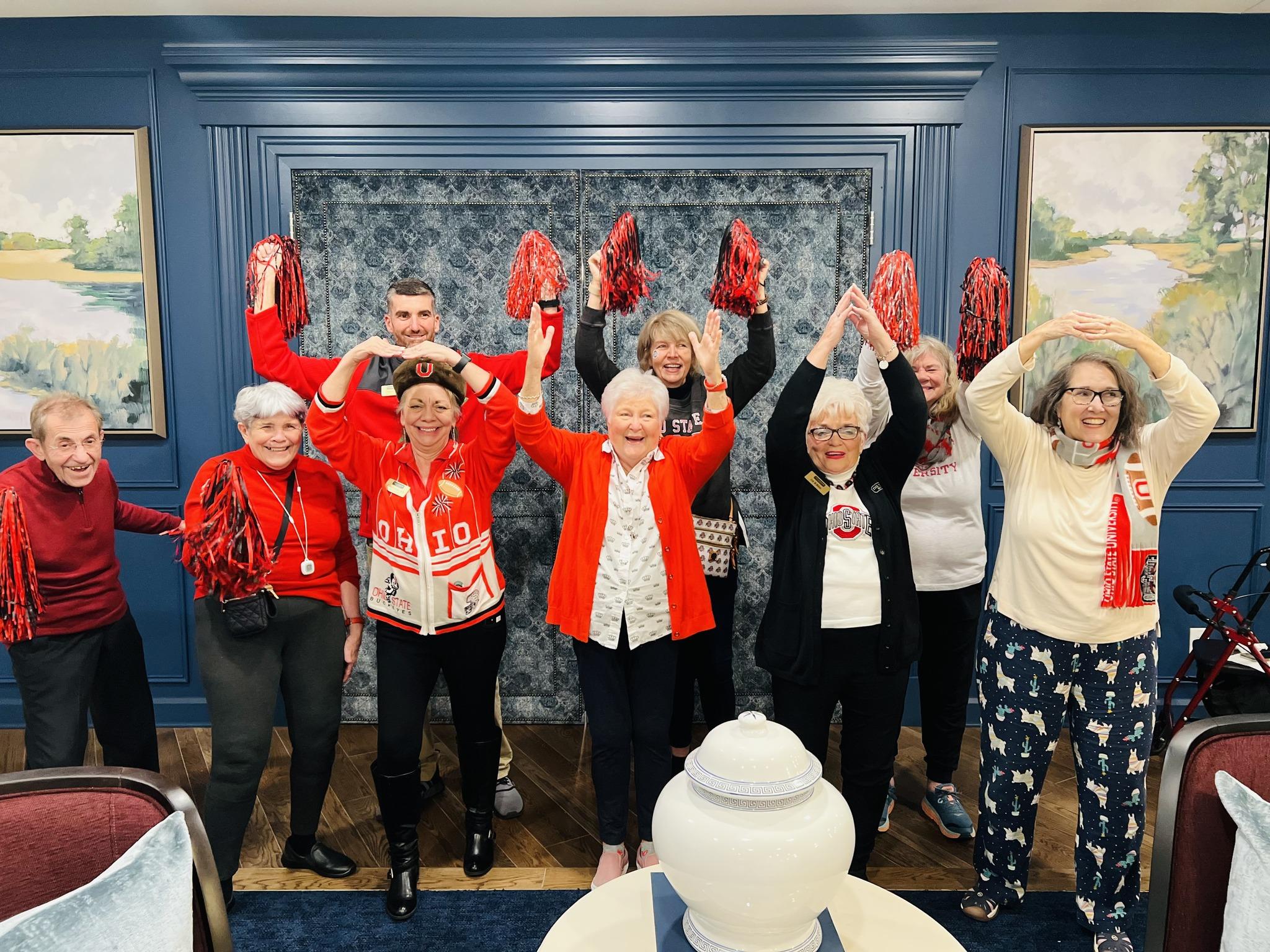 Group of cheerful adults in red and white, posing with hands raised in a celebratory gesture.