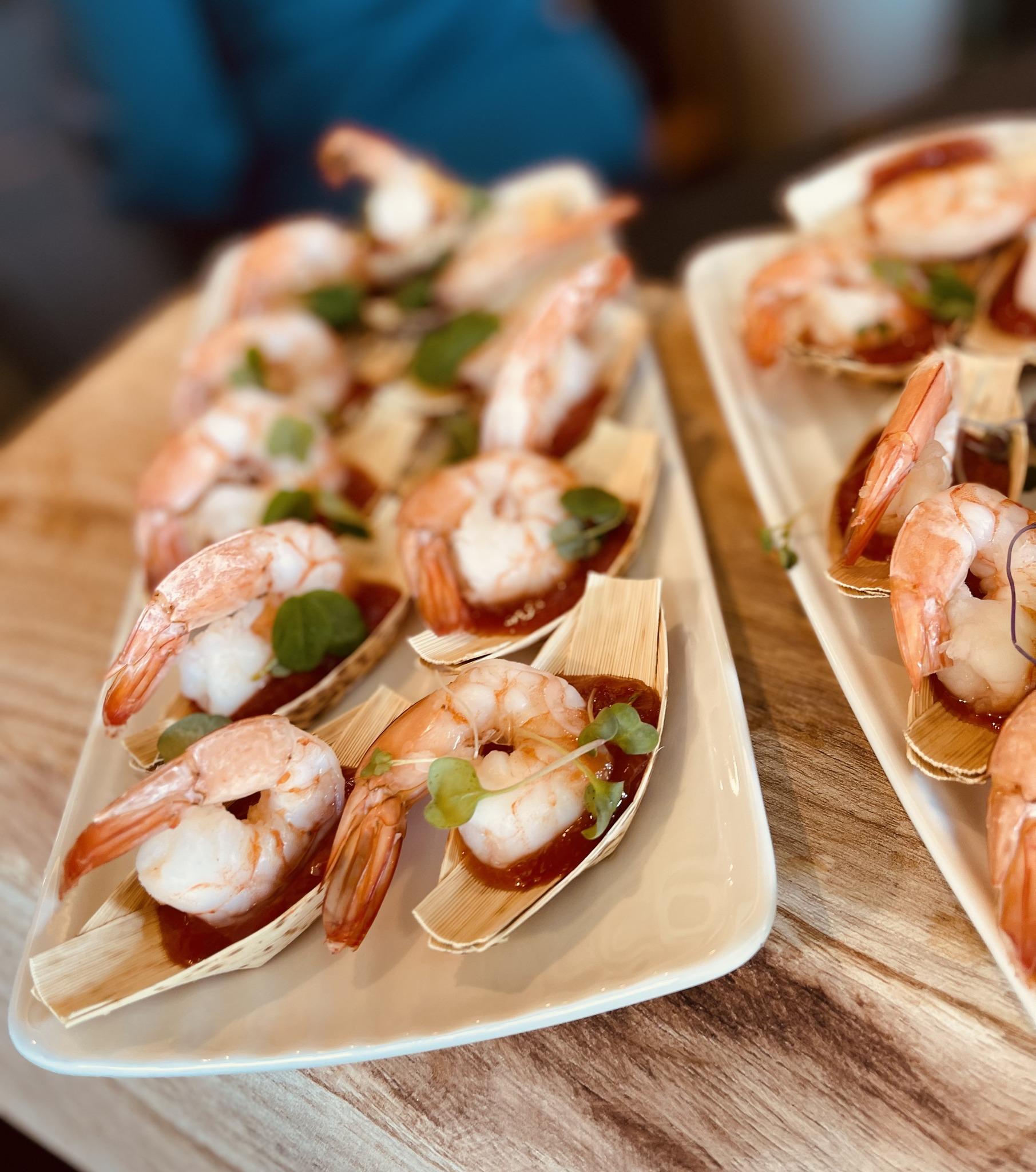 Plates of shrimp appetizers elegantly presented on small wooden boats with greens